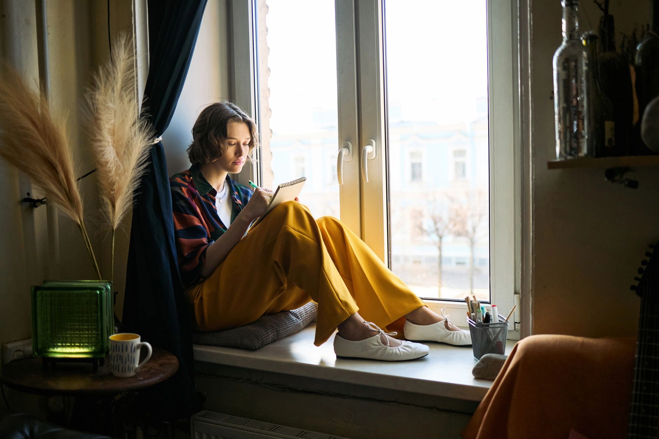 Reader writing notes in a journal by a window